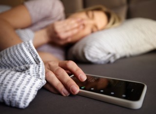 Close up of a woman turning off her alarm clock on smart phone while waking up in a bed.