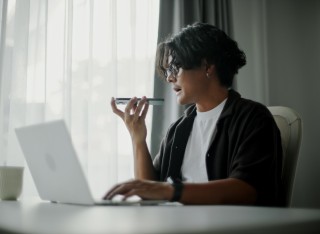 Male student using ai voice assistant while working with laptop.