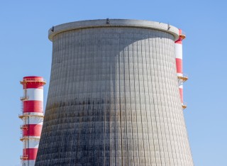 Large concrete cooling tower and red and white chimney of the carregado thermoelectric power plant in Portugal, under a clear blue sky