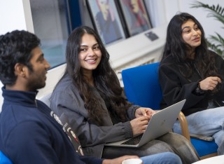 Three students sit together on chairs having a chat.