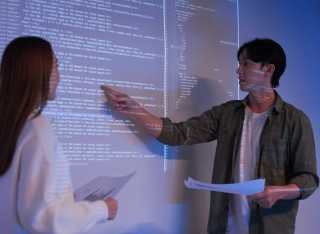Man and woman giving presentation in front of board with code