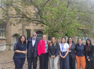 A group of men and women stand in front of a building smiling at the camera.