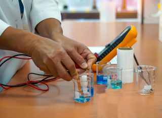 A student's hands measuring electrical currents between beakers