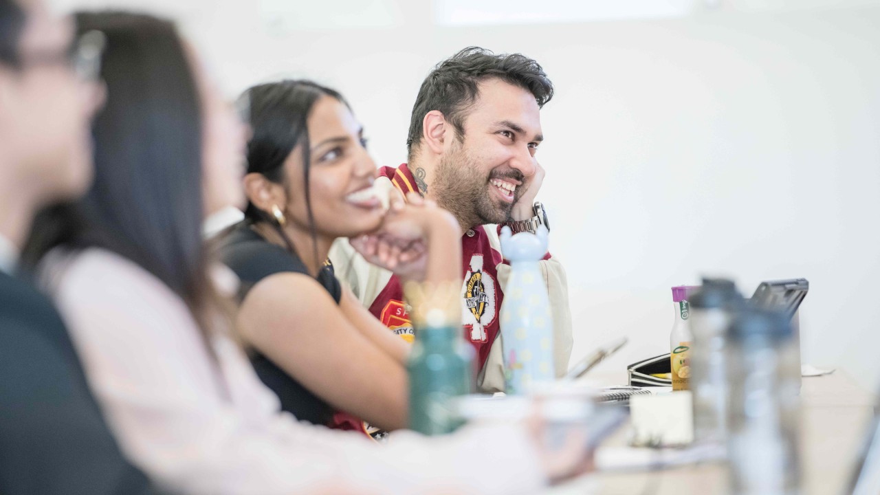 MBA students sitting at a desk smiling at unseen speaker