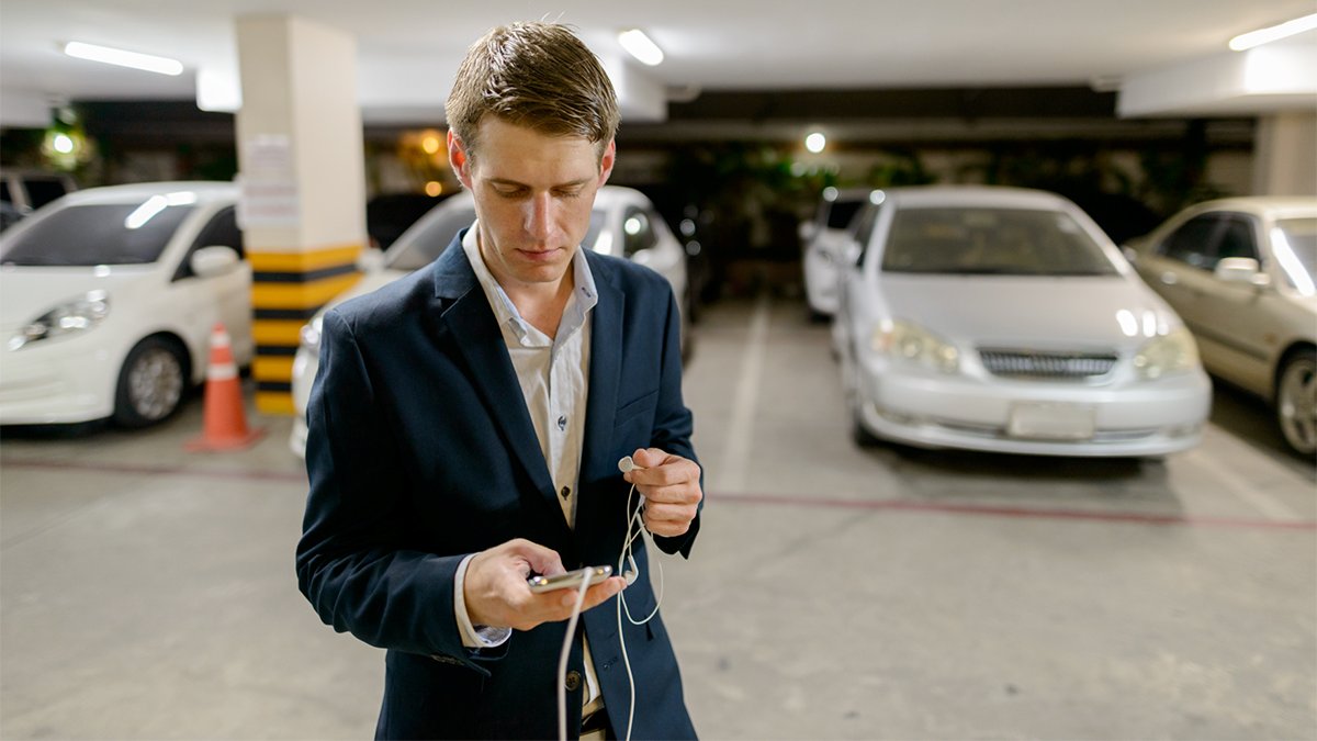 A man is looking at his phone in front of a silver car