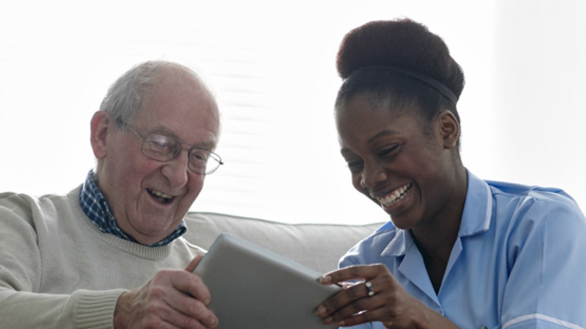 Elderly man using a tablet alongside nurse