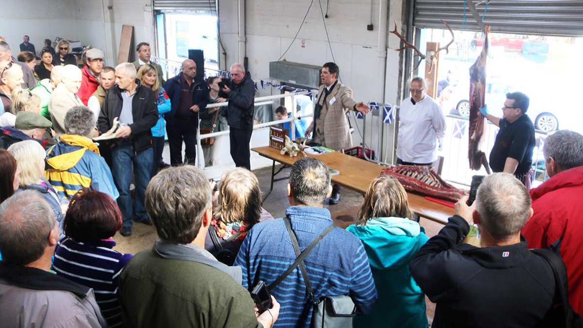 Group of people looking at cured meat on a hook
