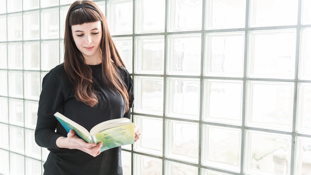 Woman reading a book near a glass panel.