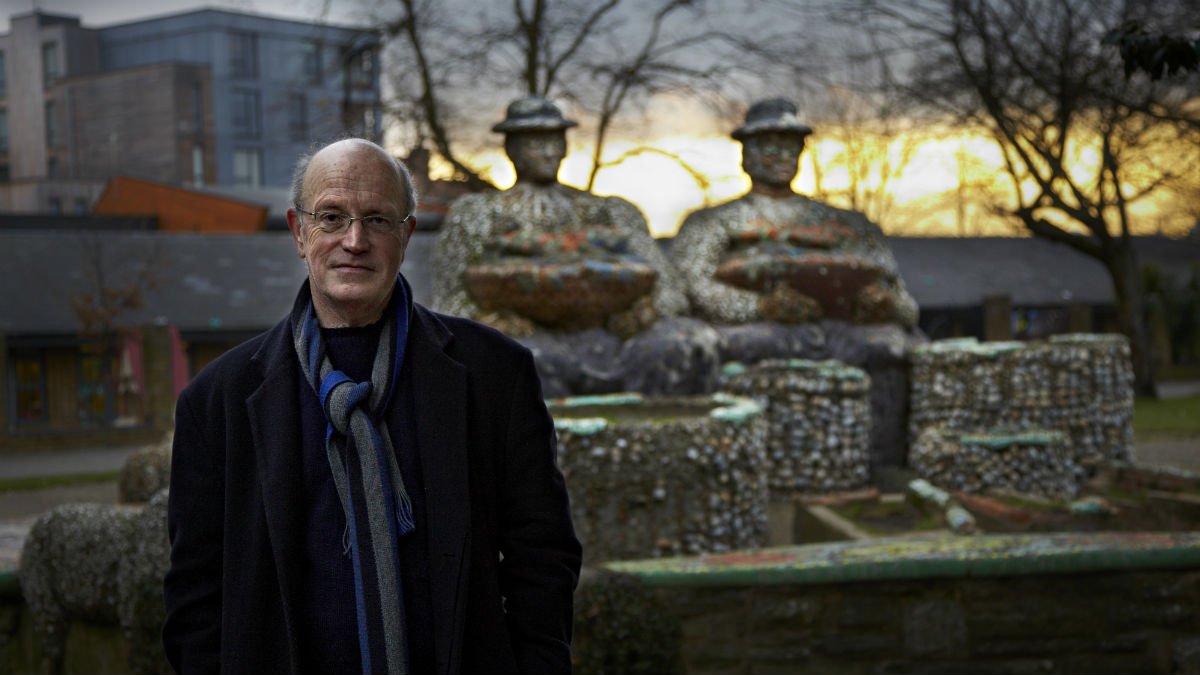 Iain Sinclair stood outside a statue and dark sky