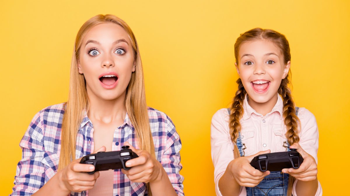 A young girl and an older girl playing computer games sat next to eachother