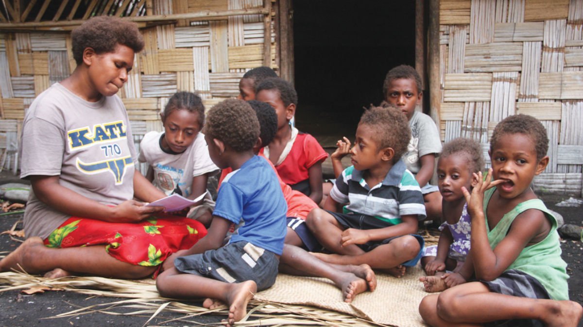 A kindergarten teacher reads stories outside to a group of Vanuatu school children
