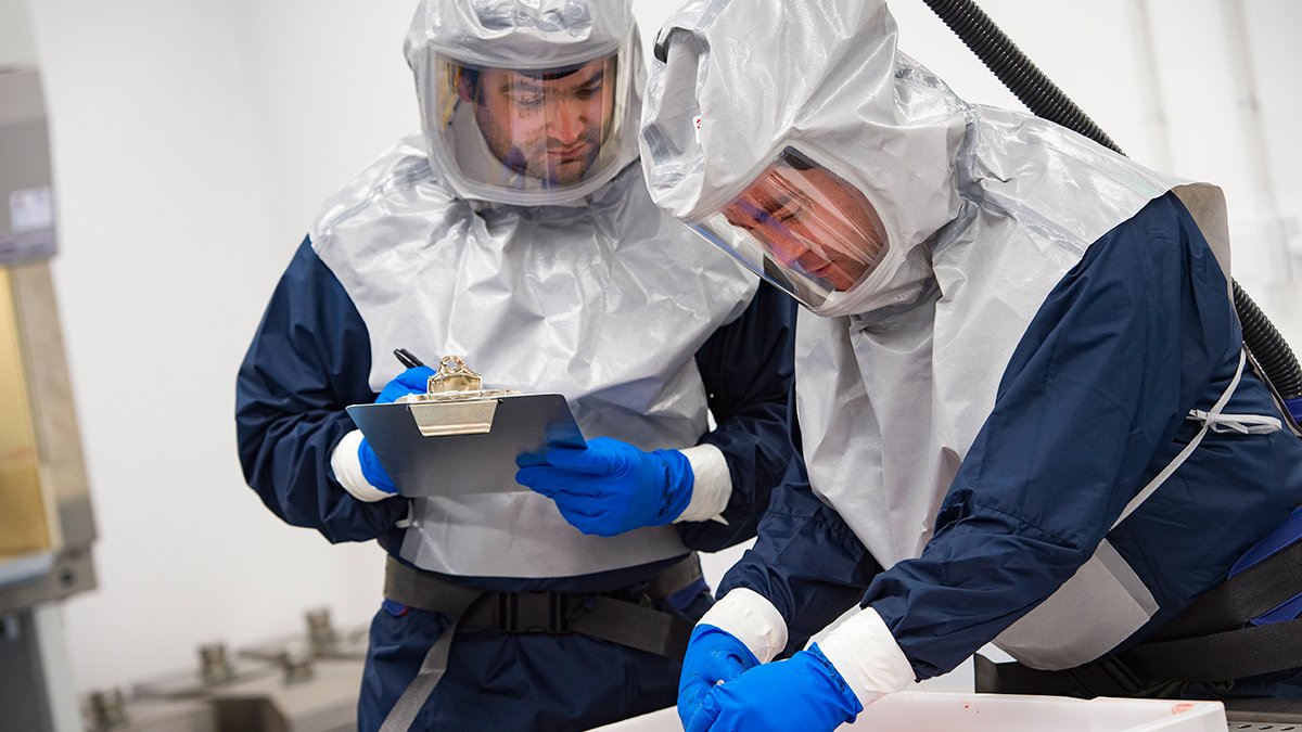 two men in hazmat suits are working in the containment level 3 room