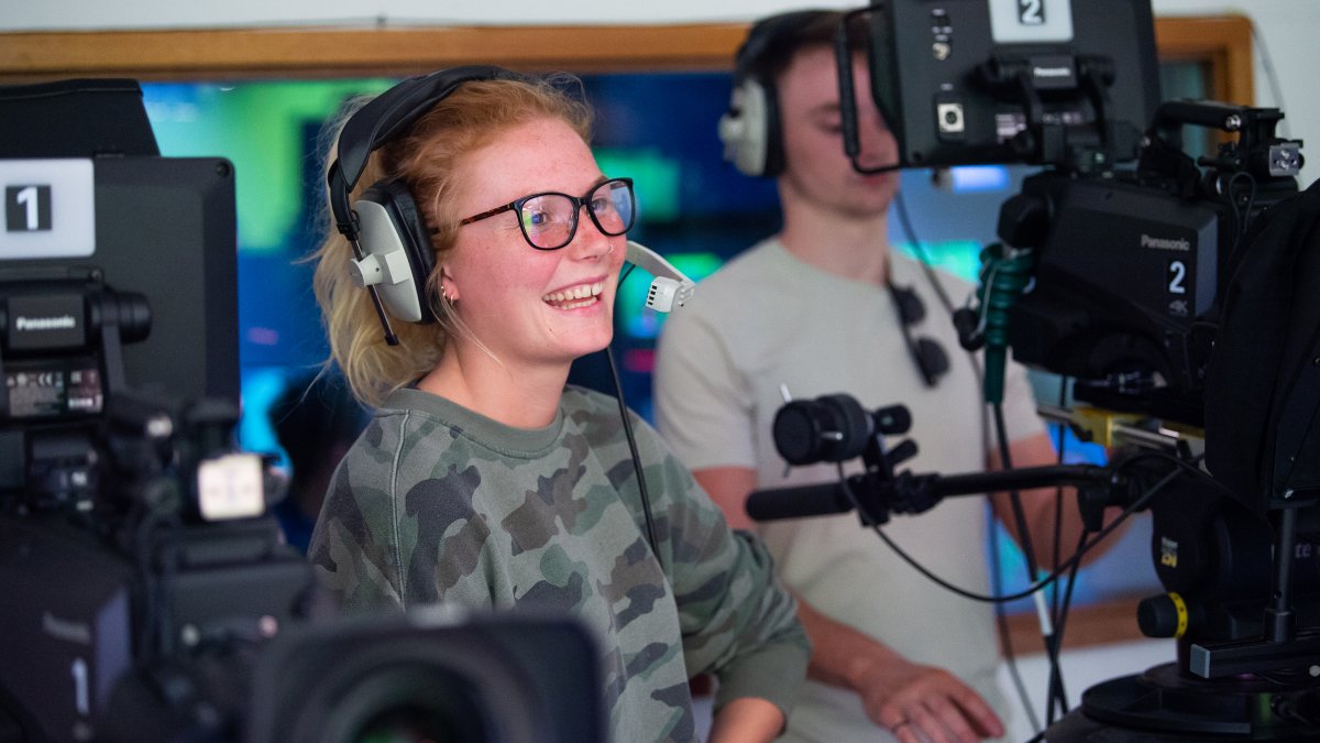 Female student smiling wearing headset in front of camera
