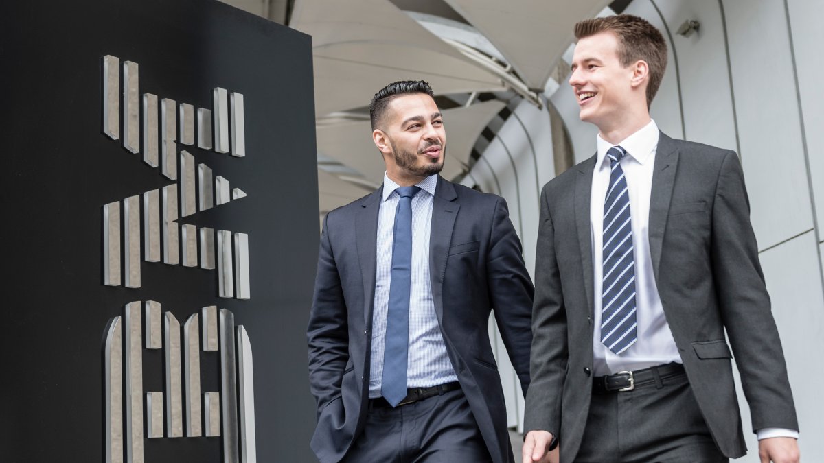 Two males in suits walking next to IBM sign.