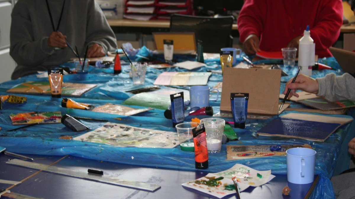 Prisoners work around a table full of colourful paint, brushes and cardboard