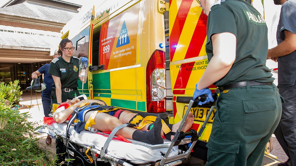 Paramedic sciences students wheeling an actor-patient into an ambulance