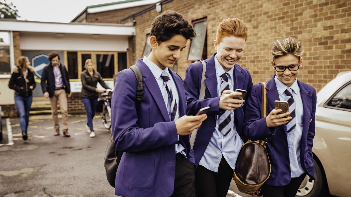 Three school boys walk and text at school