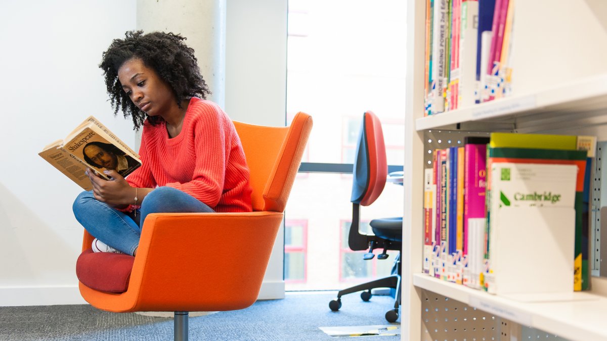 Female student reading a book sat in a chair