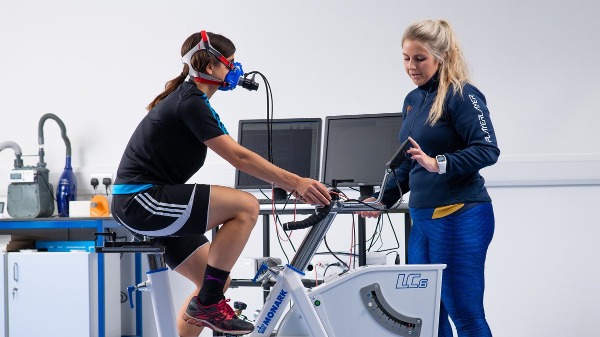 Participant cycling on exercise bike whilst staff member monitors their breathing