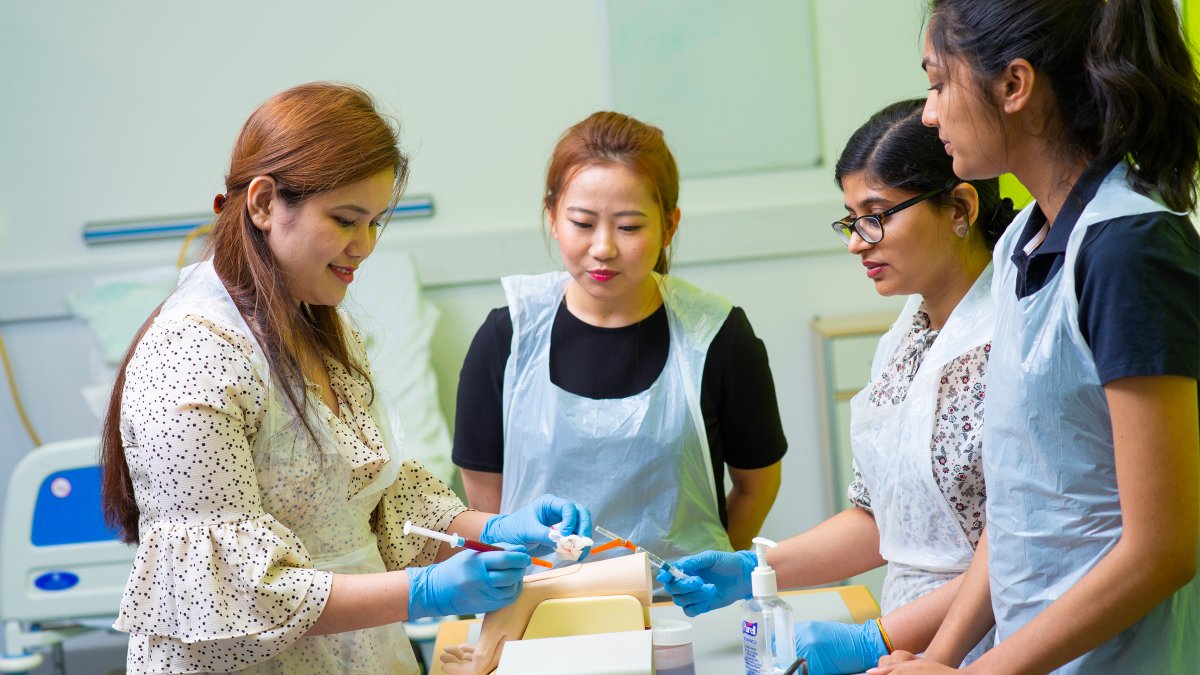 Female students practising medical procedure on dummy