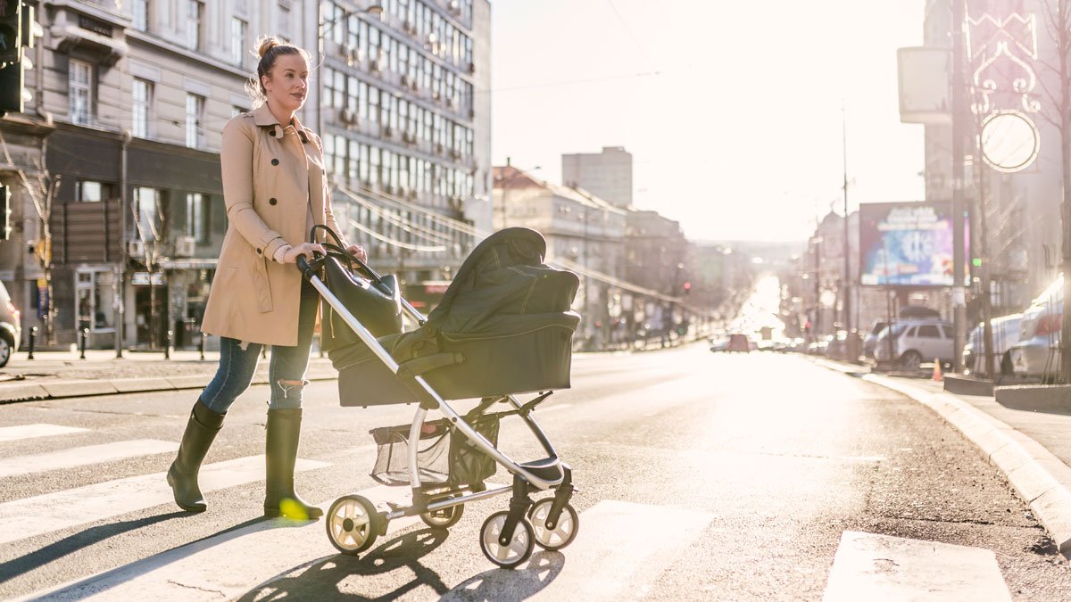 Mother pushing her baby in a pram across a road