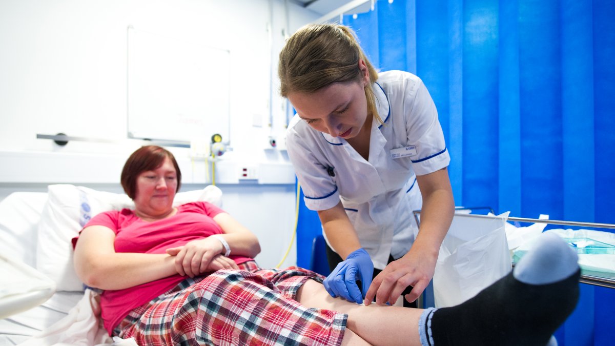 Female nursing student applying dressing to a leg wound