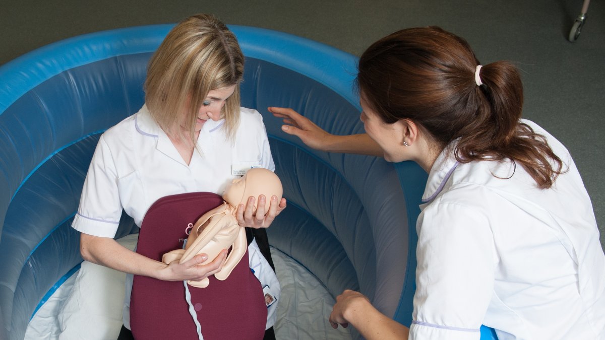 Student midwife in birthing pool holding a baby mannequin