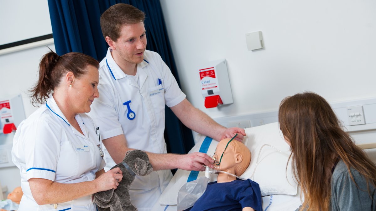 Two nursing students treating a child mannequin while talking to a parent