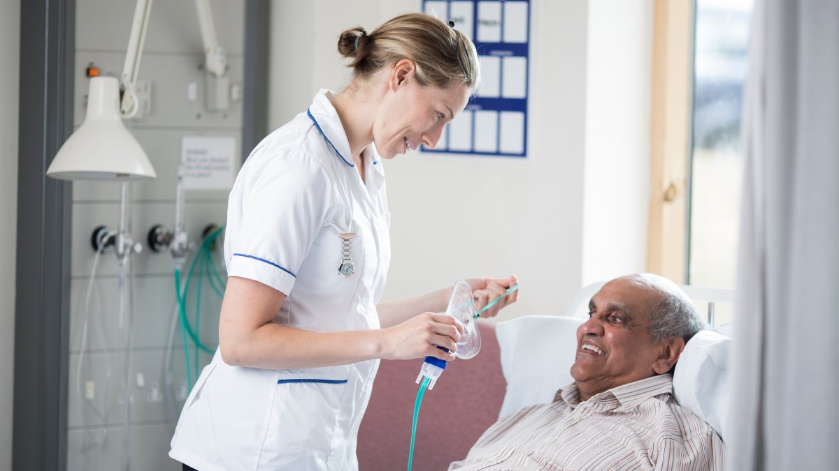 Student nurse putting breathing mask on elderly patient laying in a bed