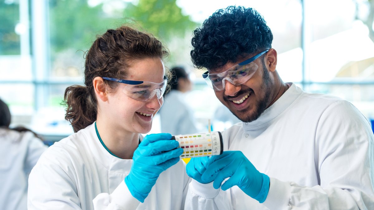 Two students holding a tub of litmus paper with pH scale on the side