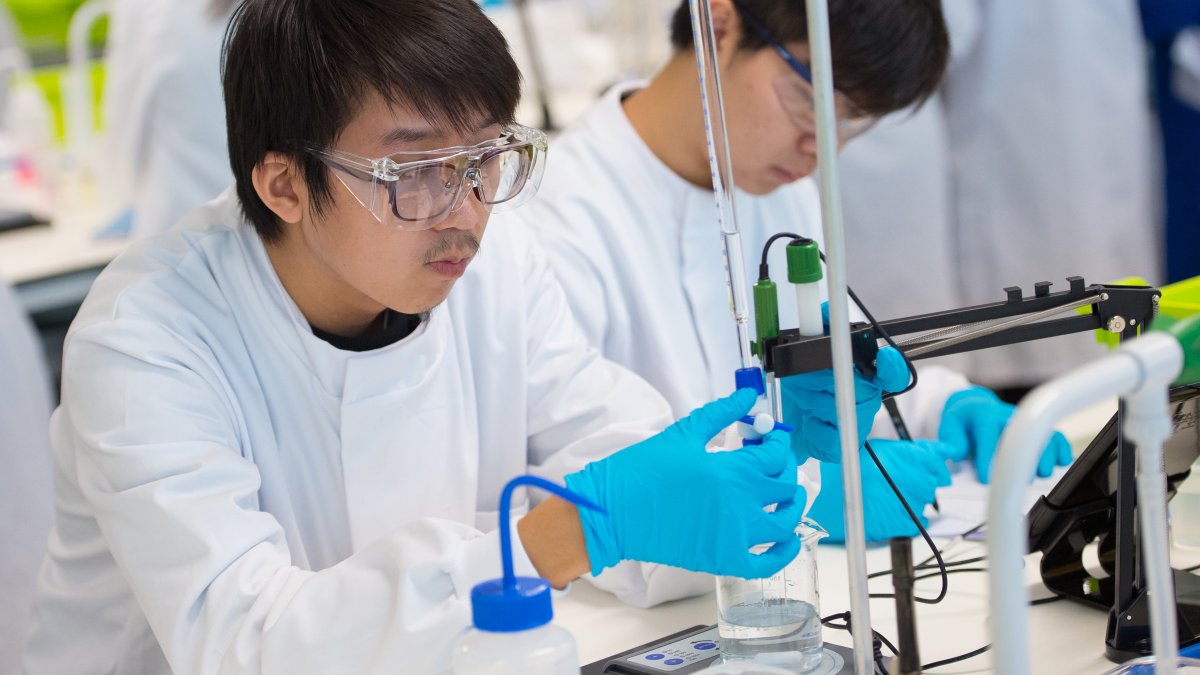 Student turning a lever to release liquid from a tube into a beaker