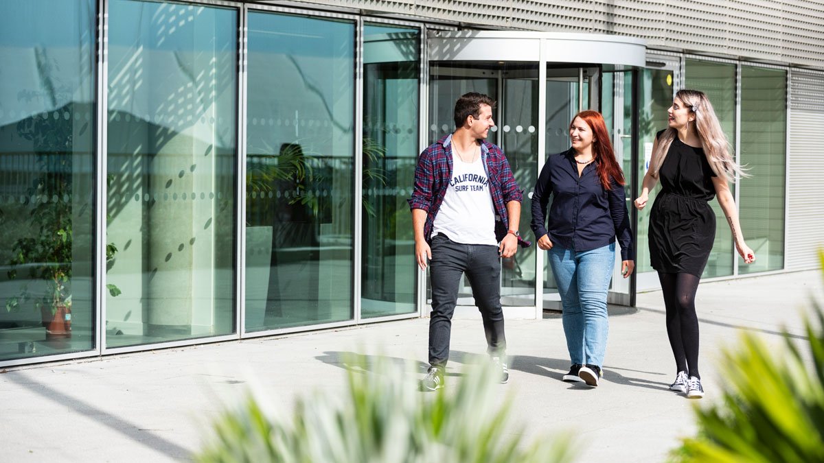 Three students walking outside the Institute for Communication Systems building