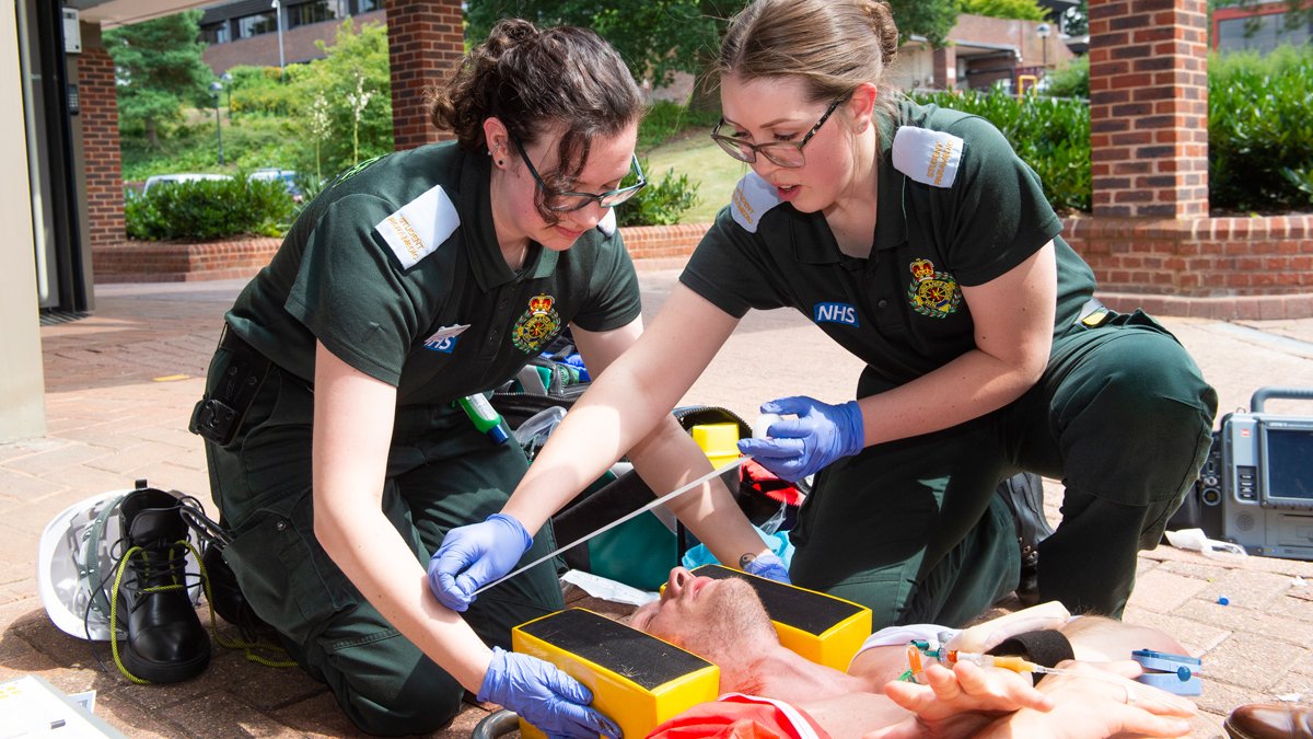 Two paramedic students holding a man's head and applying tape to secure this to a head brace