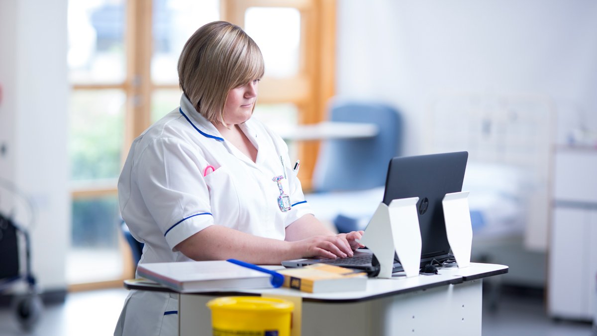 Student nurse on placement standing in front of a laptop
