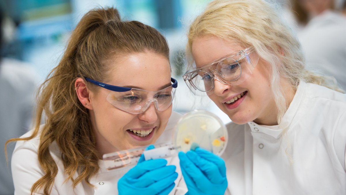 Two students holding an agar plate and measuring bacterial growth