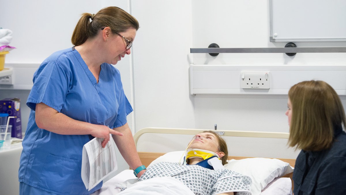 Nurse speaking to a woman wearing a neck brace, laying in a bed