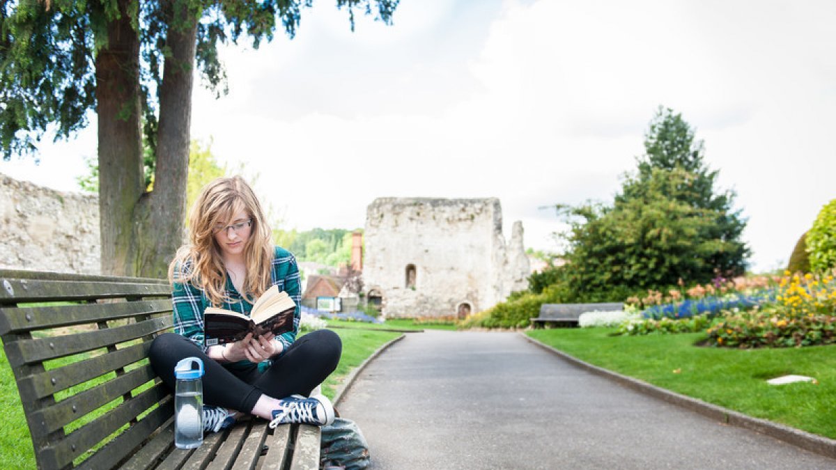 Student reading on bench in Guildford Castle grounds