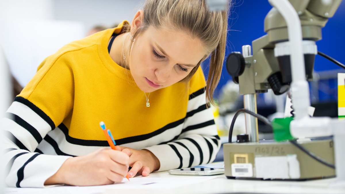 Student writing on a piece of paper next to a microscope