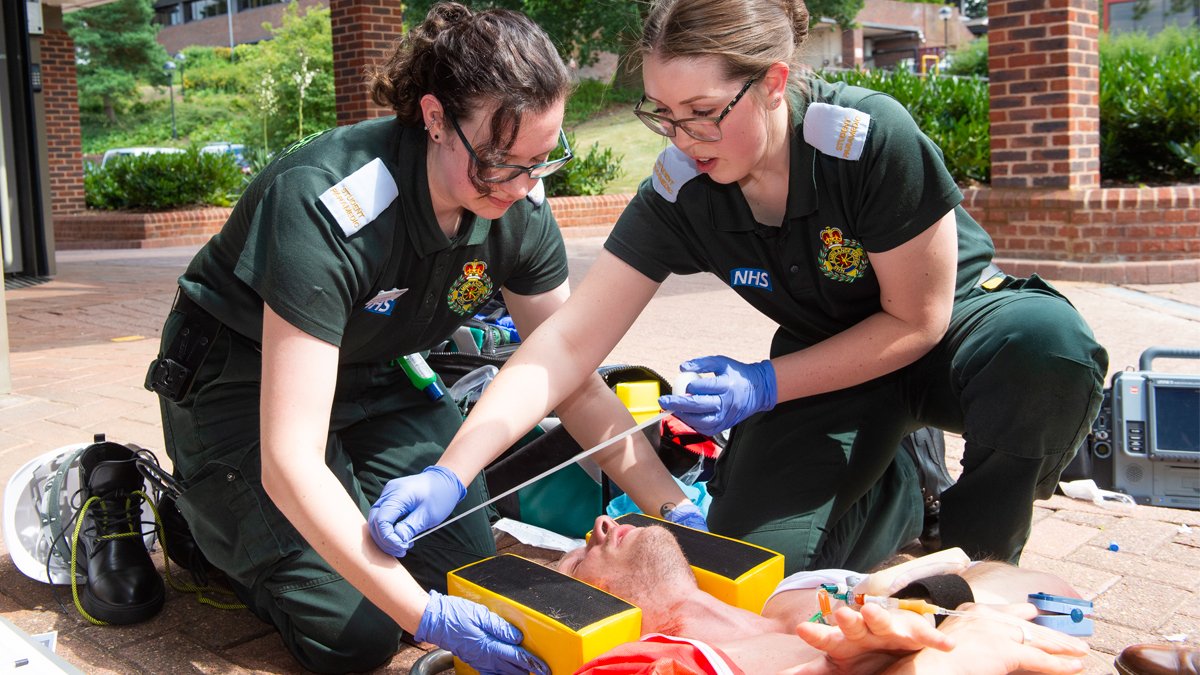 Two trainee paramedics providing medical care to patient strapped to a board