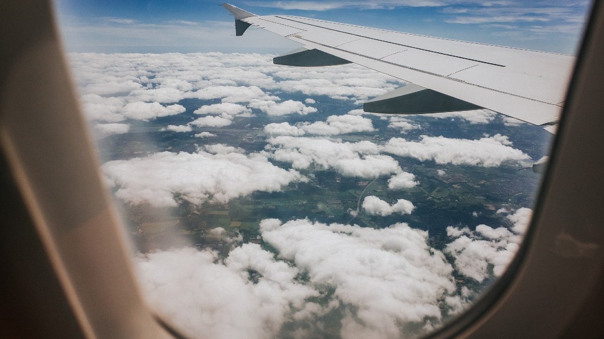 The view of clouds and an aircraft's wing, seen through the oval window of a plane from the interior