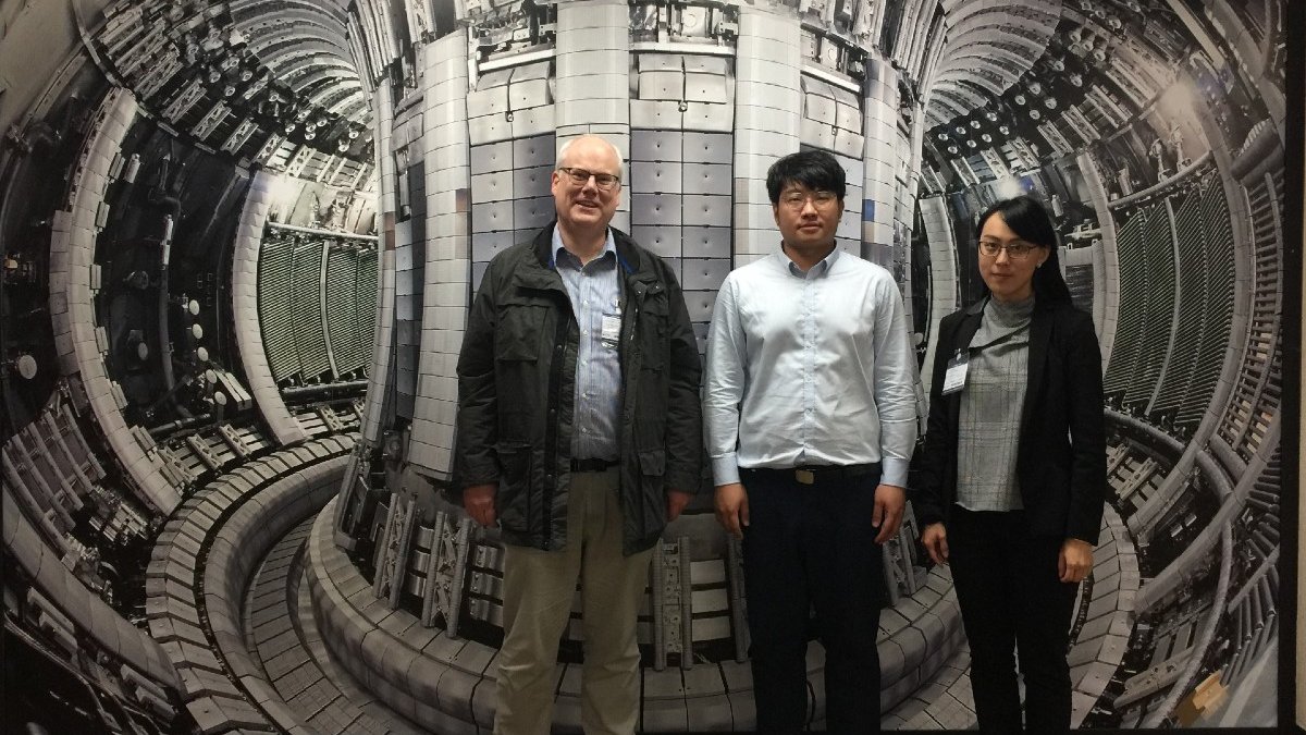 Three scientists stand in front of an image of a nuclear reactor