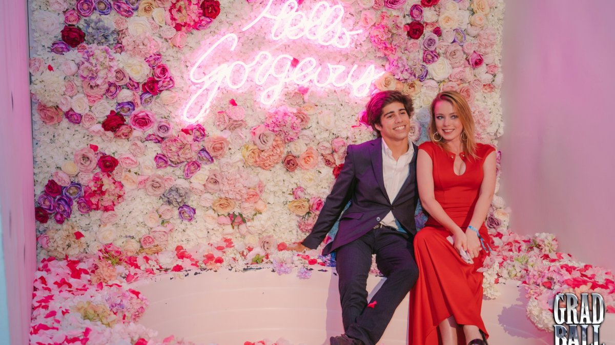 Two graduates sitting in a flowery photobooth at Graduation Ball