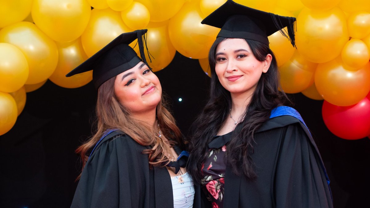 Two graduates standing in front of a balloon arch at the reception