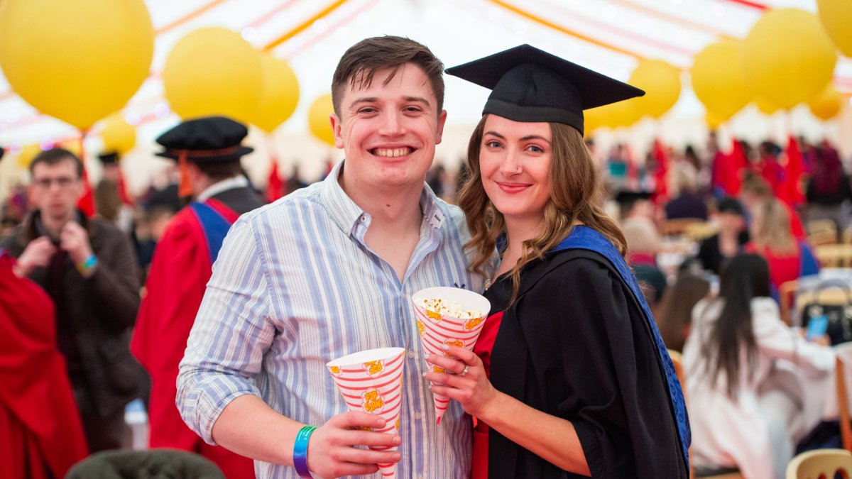 A graduate and their guest at the reception holding popcorn