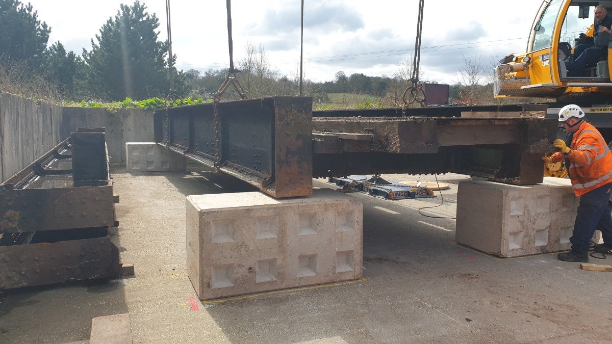 Section of railway bridge being loaded onto raised blocks by crane