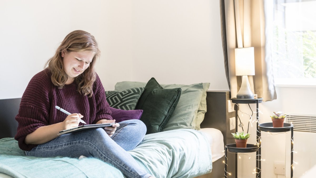 Student writes whilst sat on bed