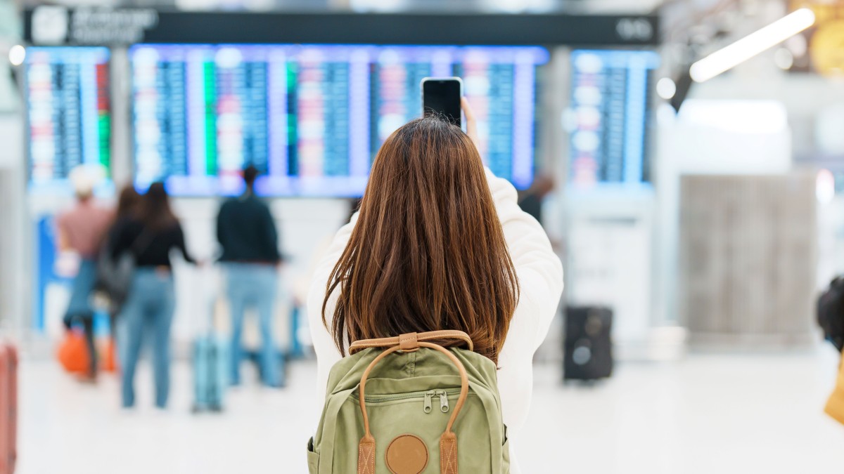 Young women taking photo of departures board with mobile phone
