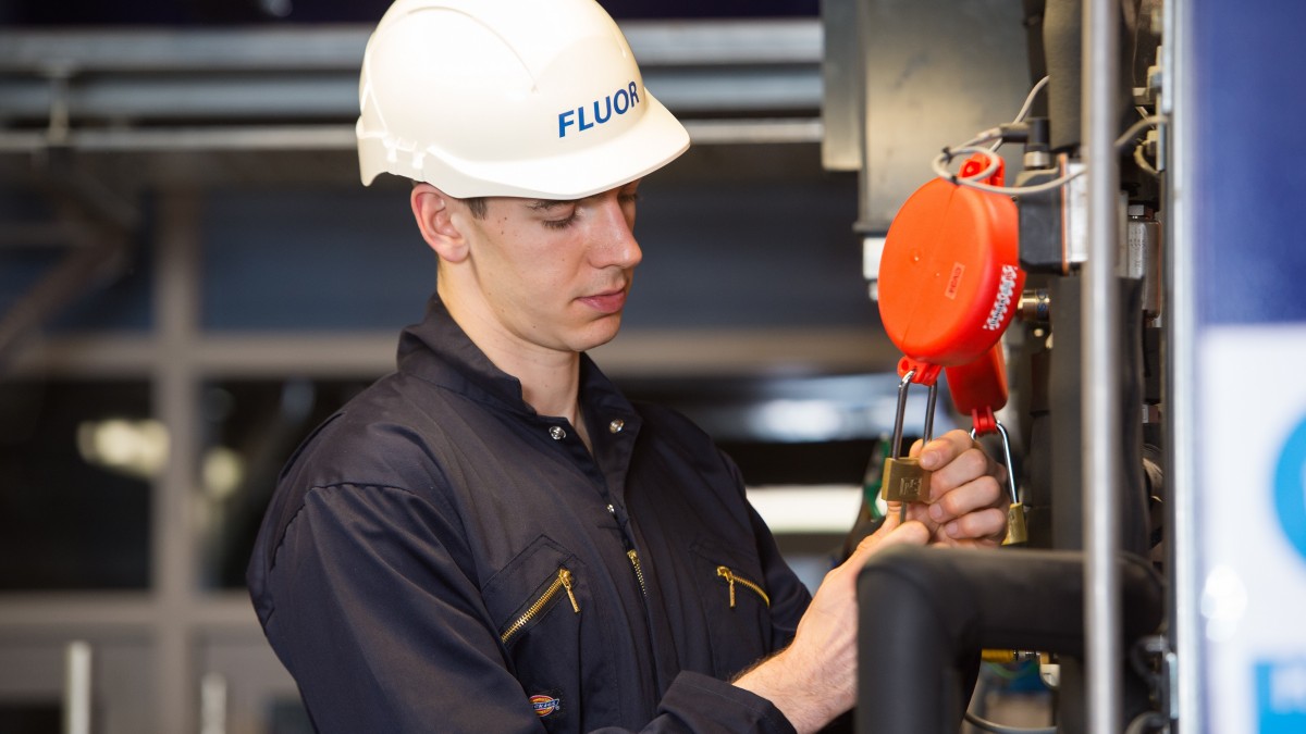 A chemical engineering student with a white hard hat on secures a padlock in the Fluor Pilot Plant.