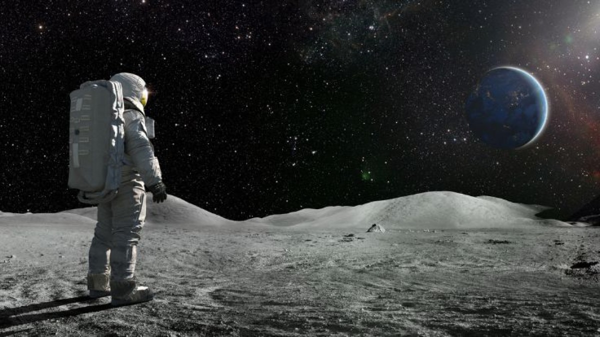 An astronaut stands on the surface of the moon looking at Earth