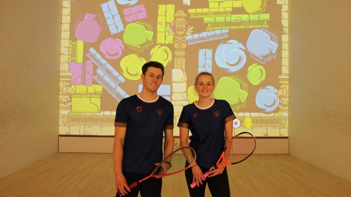 Two Students posing in front of the new interactive Squash Wall